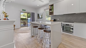 A modern kitchen with white cabinetry, a central island with stools, a built-in oven, and a ceiling fan. - Blue Summit Hideaway (Yungaburra)