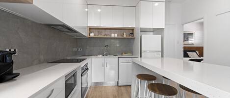 Una cocina moderna con armarios blancos, encimera de madera, horno empotrado y cafetera.
