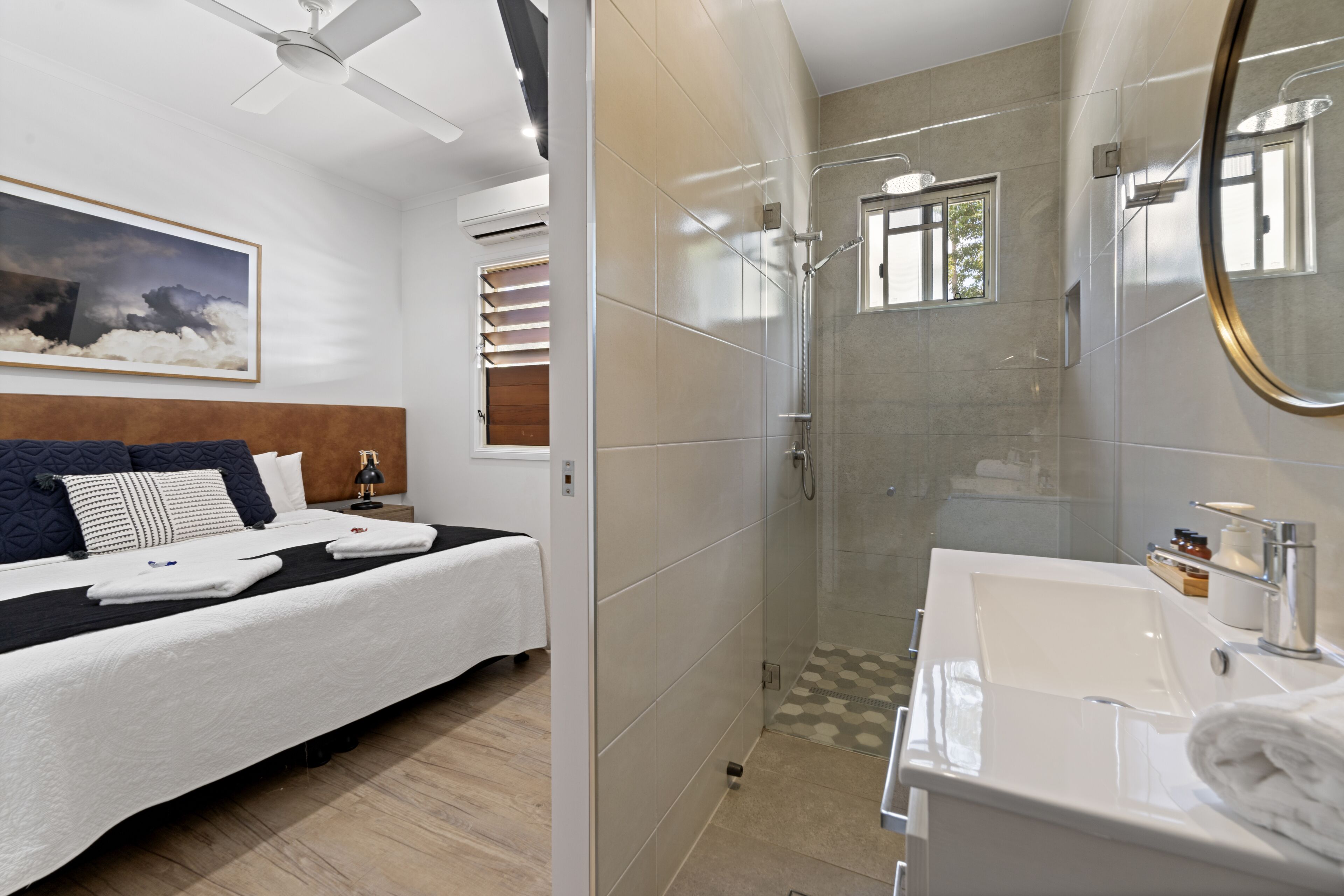 A modern hotel room with a large bed, a shower area, and a bathroom with a sink and mirror.