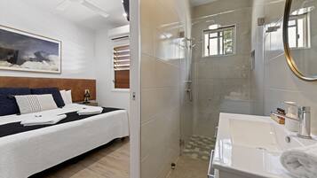 A modern hotel room with a large bed, a shower area, and a bathroom with a sink and mirror.