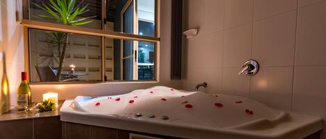 A modern bathroom with a large bathtub, a window, and a potted plant.