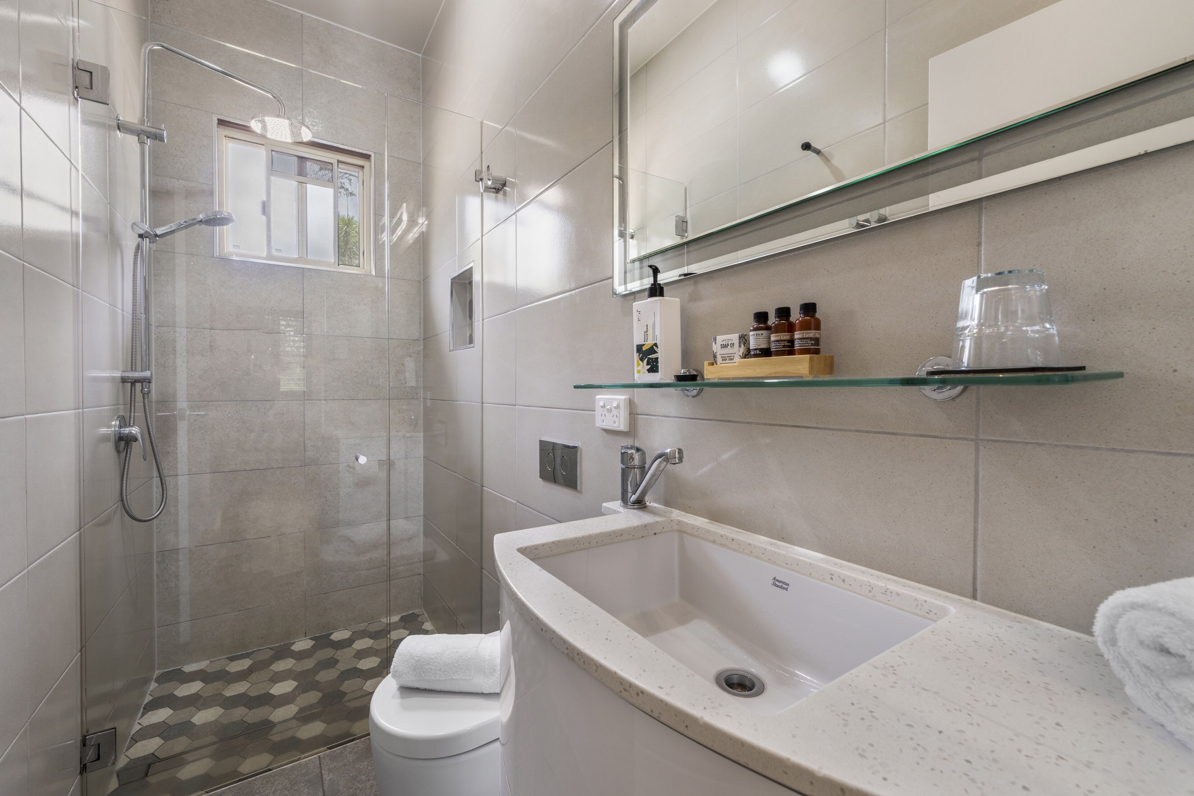 A modern bathroom with a glass shower enclosure, a white toilet, a sink with a speckled countertop, and a mirror above the sink.