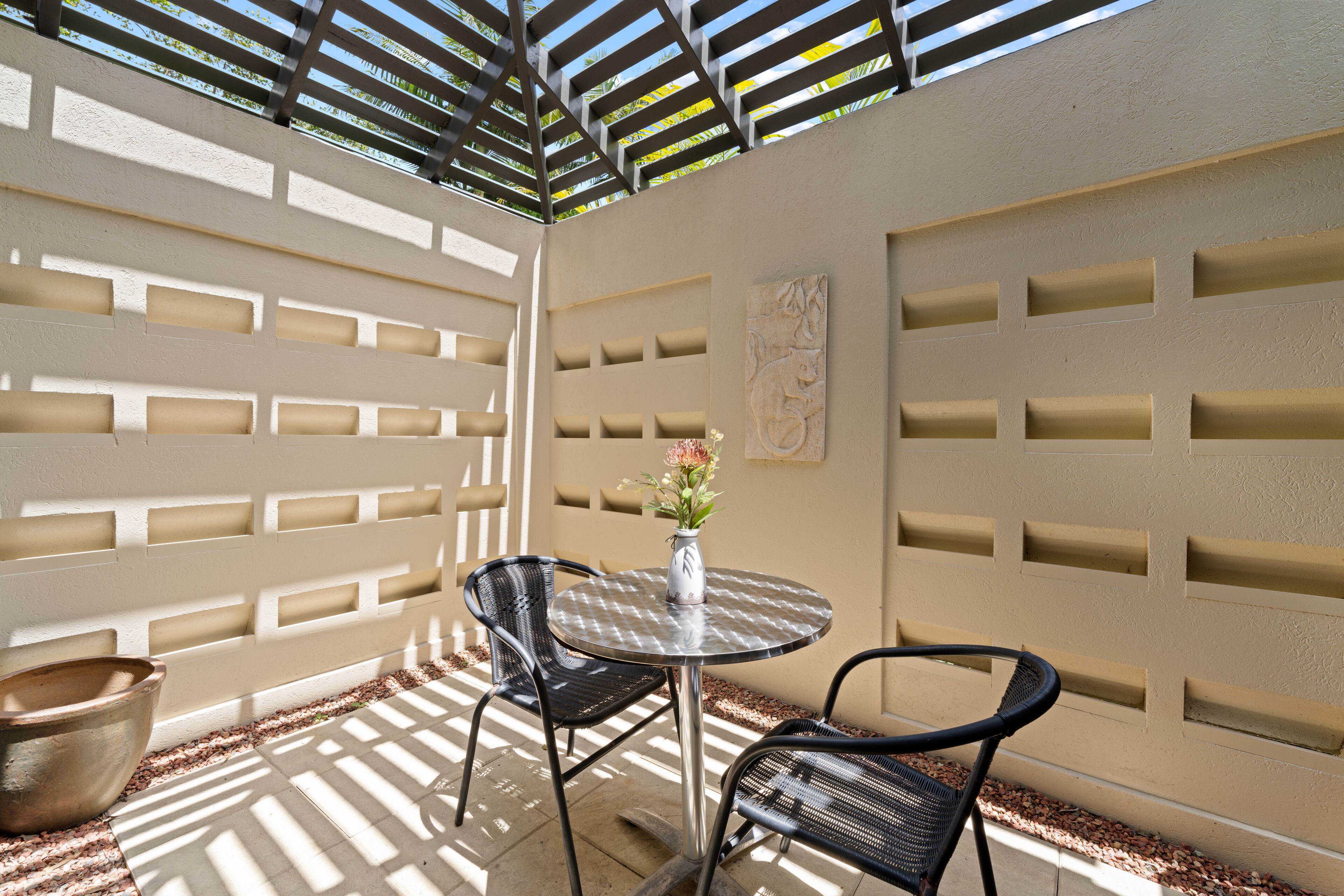 A patio with a round table and two chairs, a vase with flowers, and a decorative wall with geometric patterns.