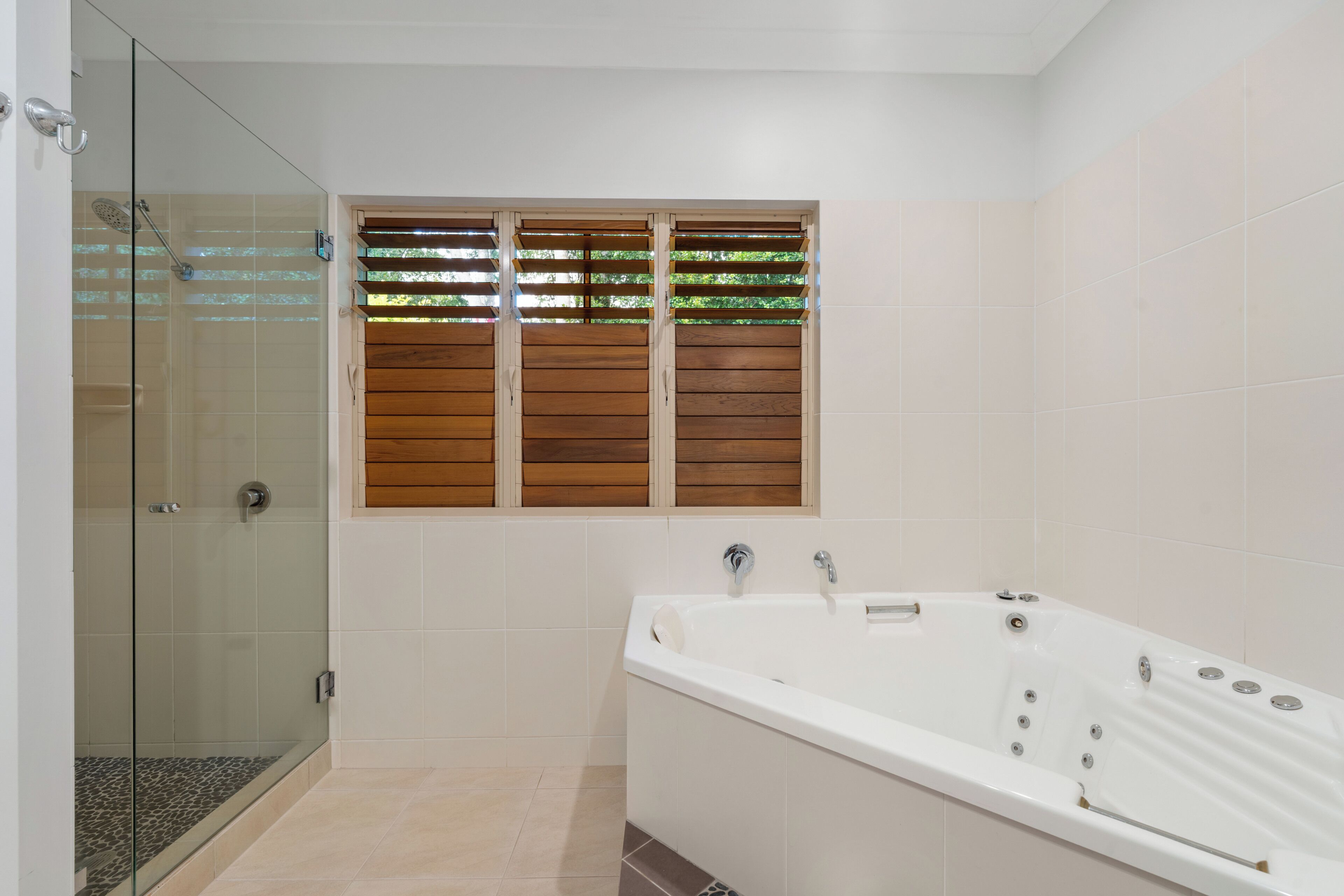 A bathroom with a glass shower enclosure, a bathtub, and wooden window shutters.
