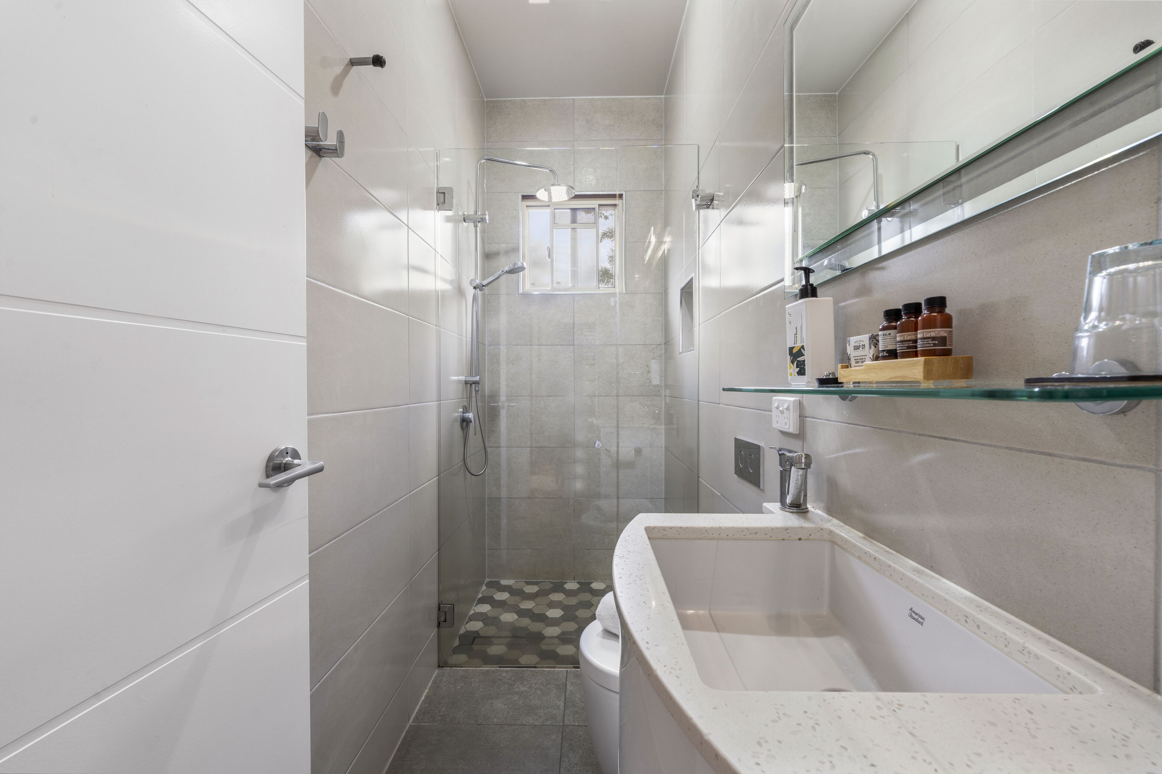 A modern bathroom with a glass shower enclosure, a white sink, and a glass shelf with toiletries.