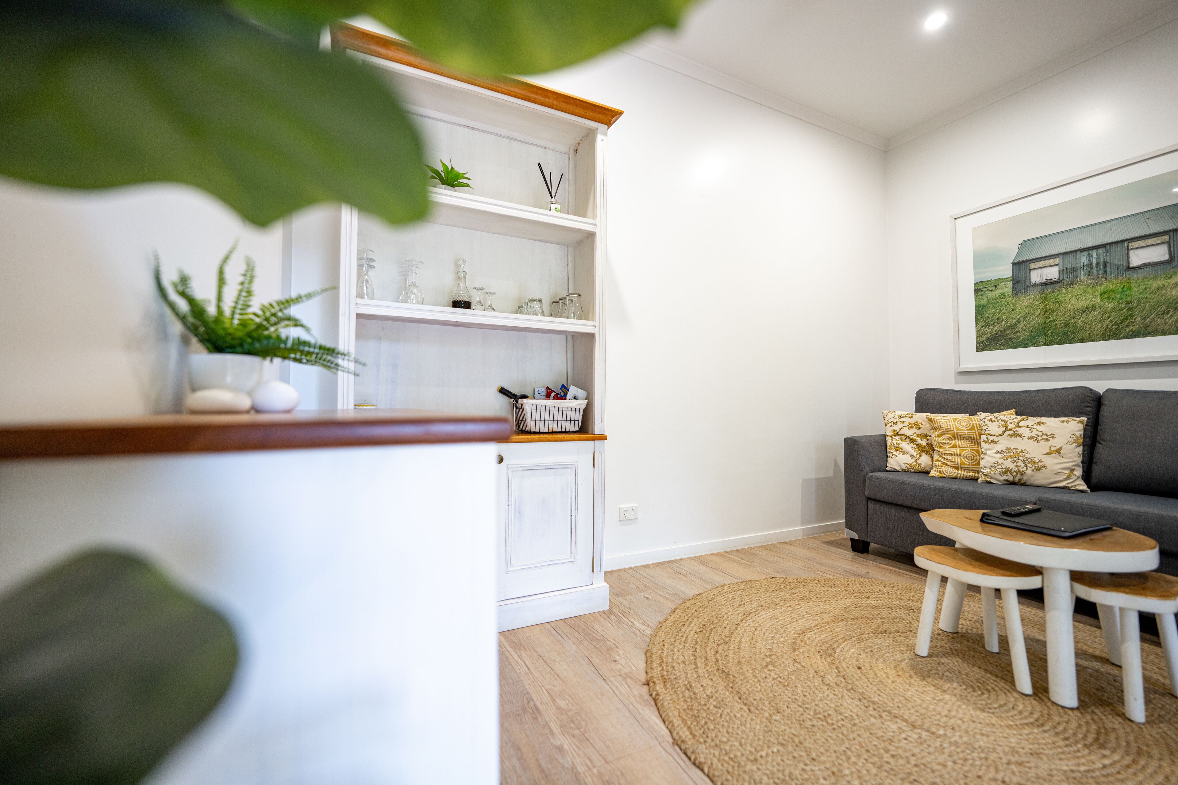 A modern living room with a sofa, a small coffee table, and a kitchen area with shelves.