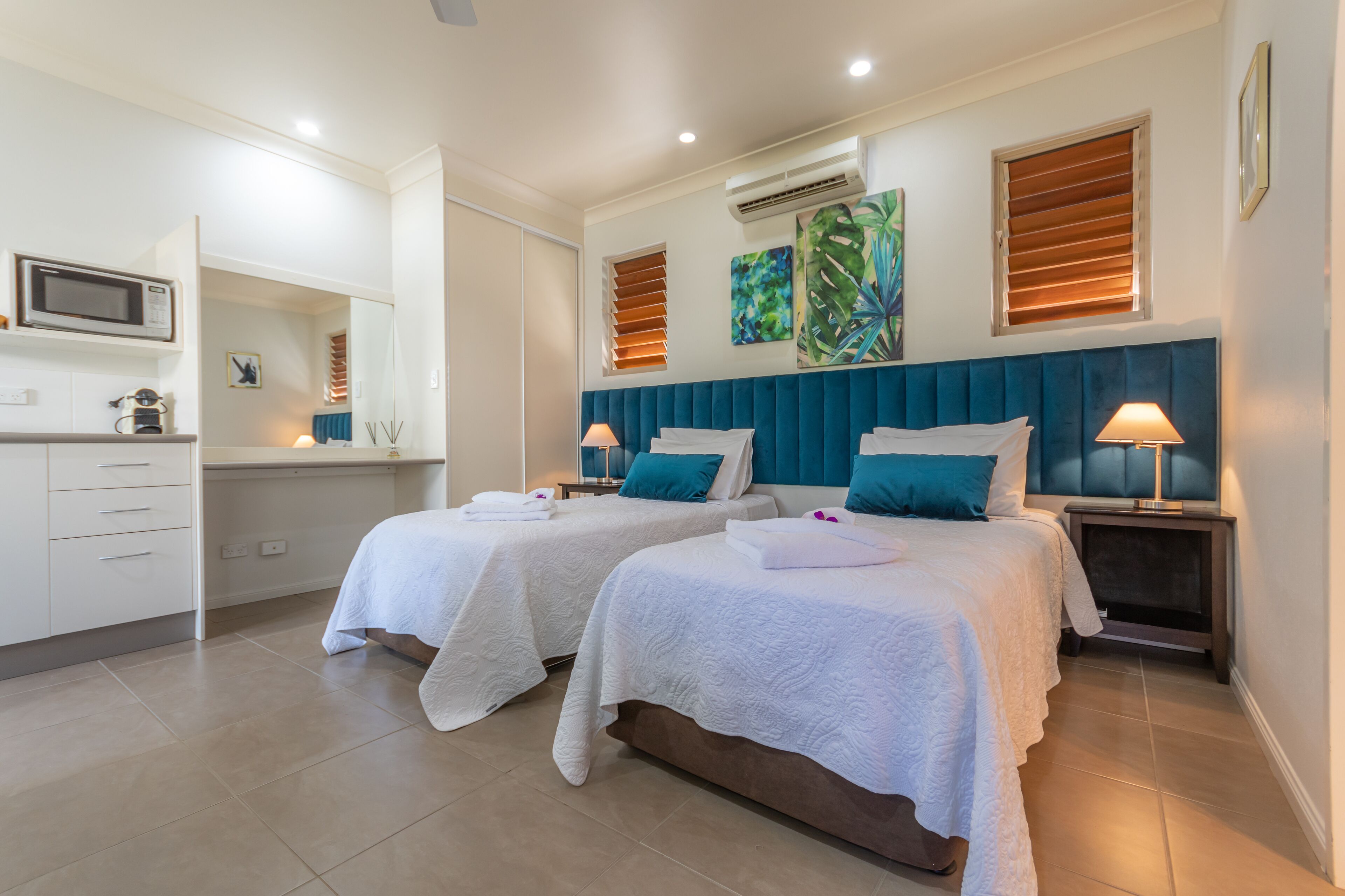 Une chambre d’hôtel avec deux lits, un four à micro-ondes, un petit bureau et une fenêtre avec des stores.
