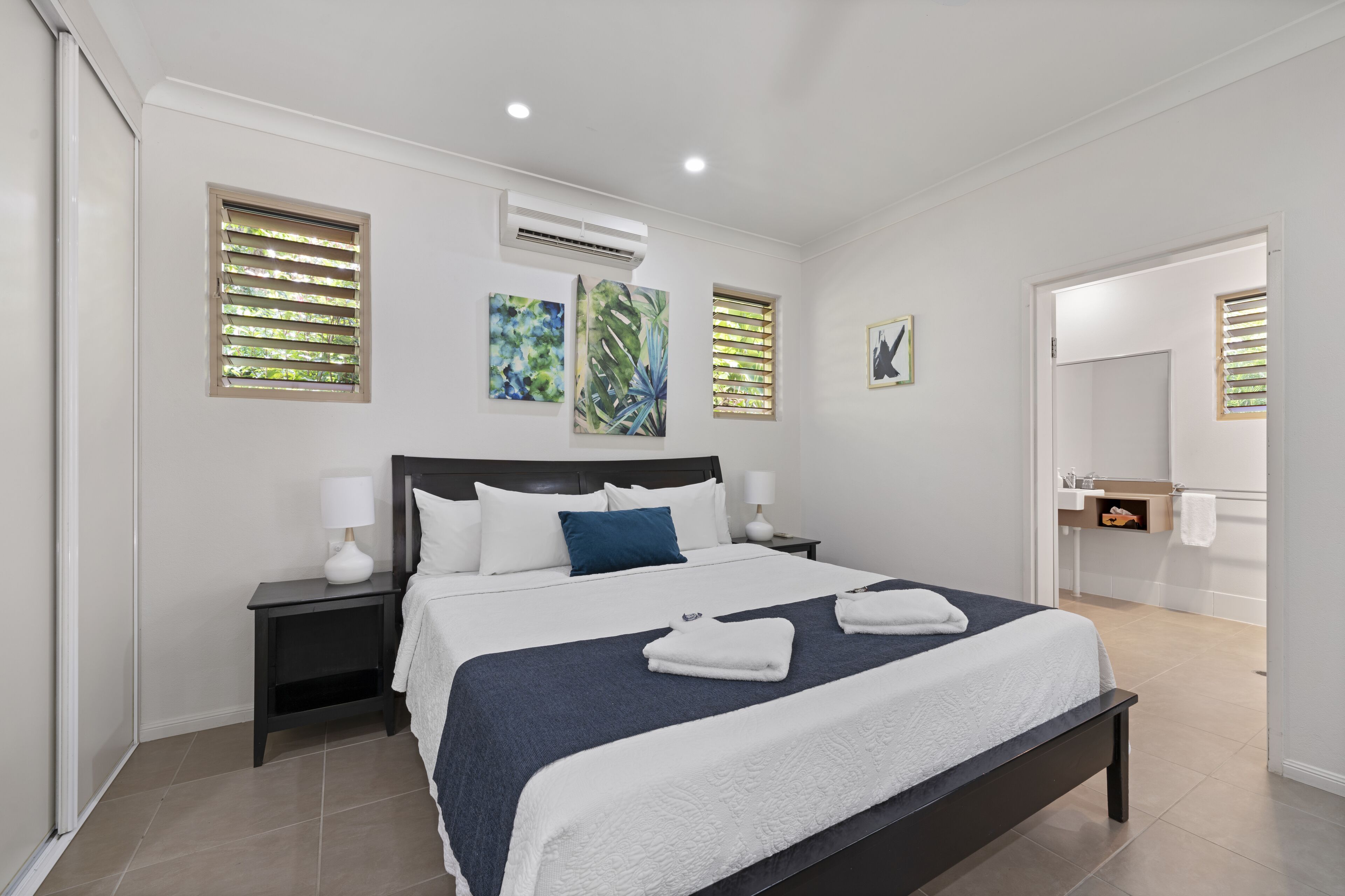 A modern hotel room with a large bed, two bedside tables, an air conditioning unit, and artwork on the walls.