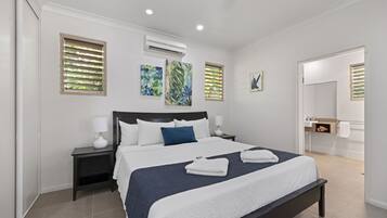 A modern hotel room with a large bed, two bedside tables, an air conditioning unit, and artwork on the walls.