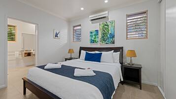 A modern hotel room with a large bed, two bedside tables with lamps, a bathroom visible through an open door, and artwork on the walls.
