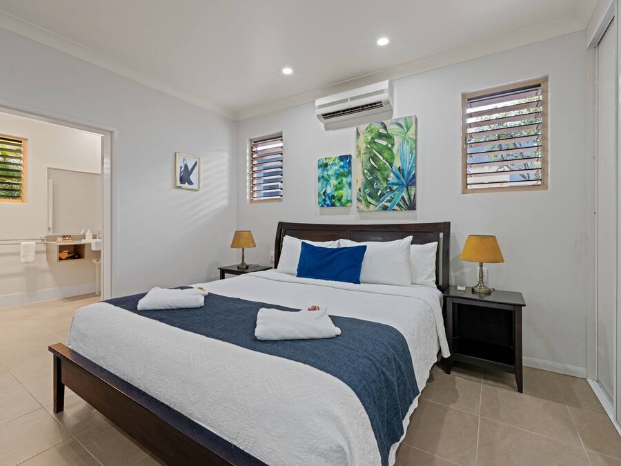 A modern hotel room with a large bed, two bedside tables with lamps, a bathroom visible through an open door, and artwork on the walls.