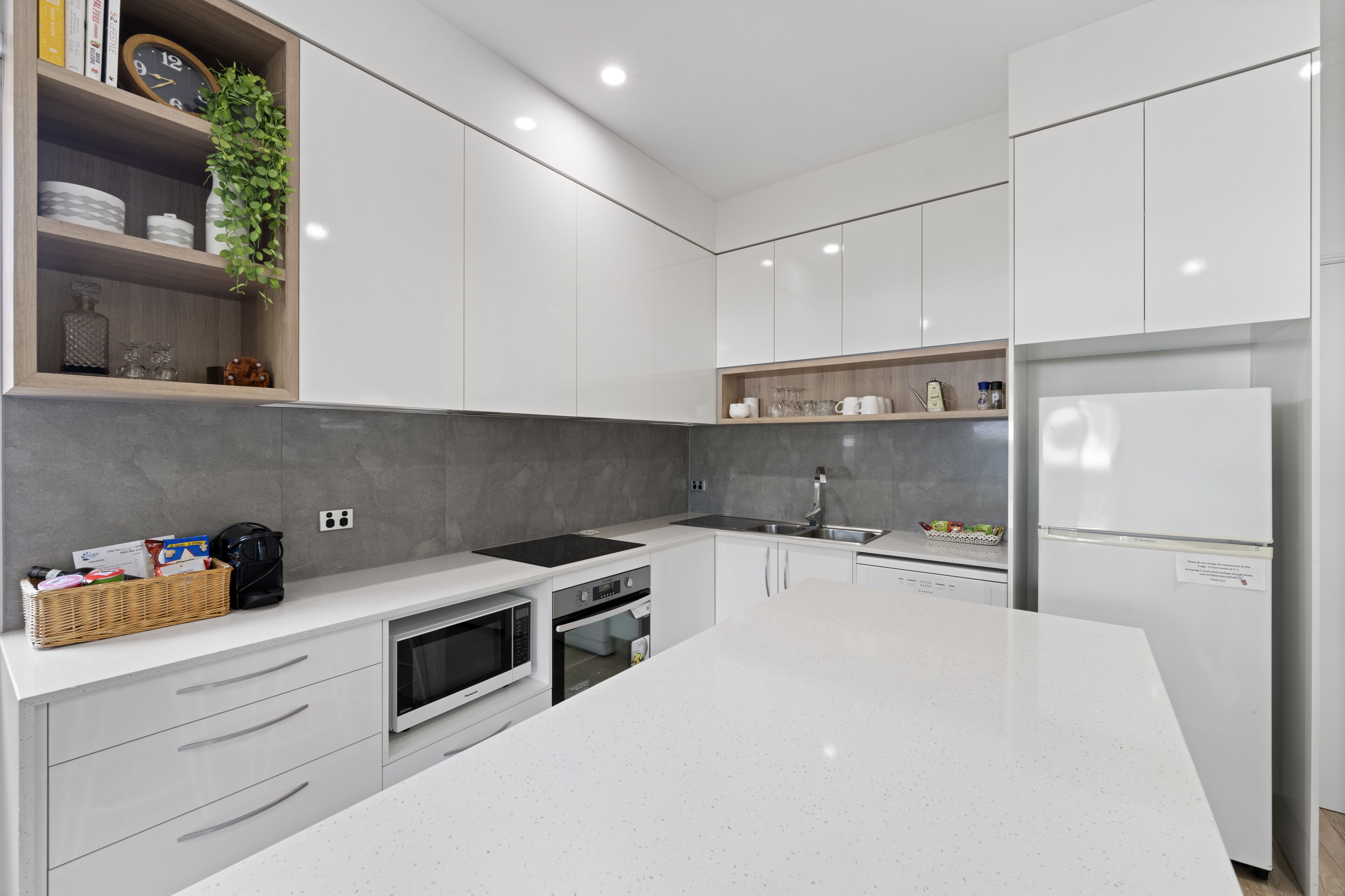 A modern kitchen with white cabinetry, a central island, built-in appliances, and a hanging plant.