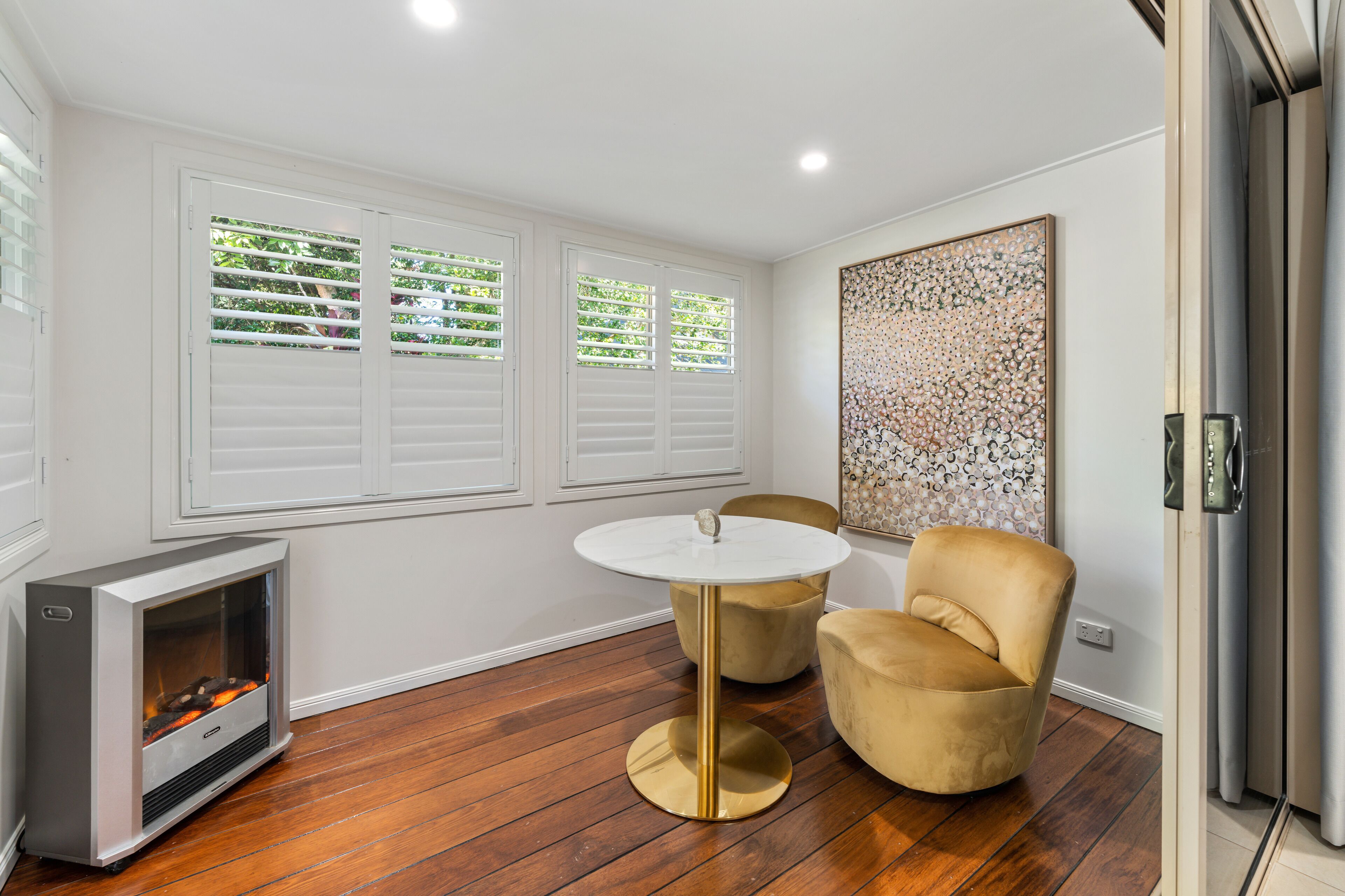 A modern room with a fireplace, two chairs, a round table, and a large abstract painting on the wall.