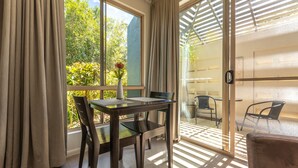 A room with a dining table, chairs, a vase with flowers, and a view of greenery outside. - Blue Summit Hideaway (Yungaburra)