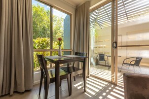 A room with a dining table, chairs, a vase with flowers, and a view of greenery outside.