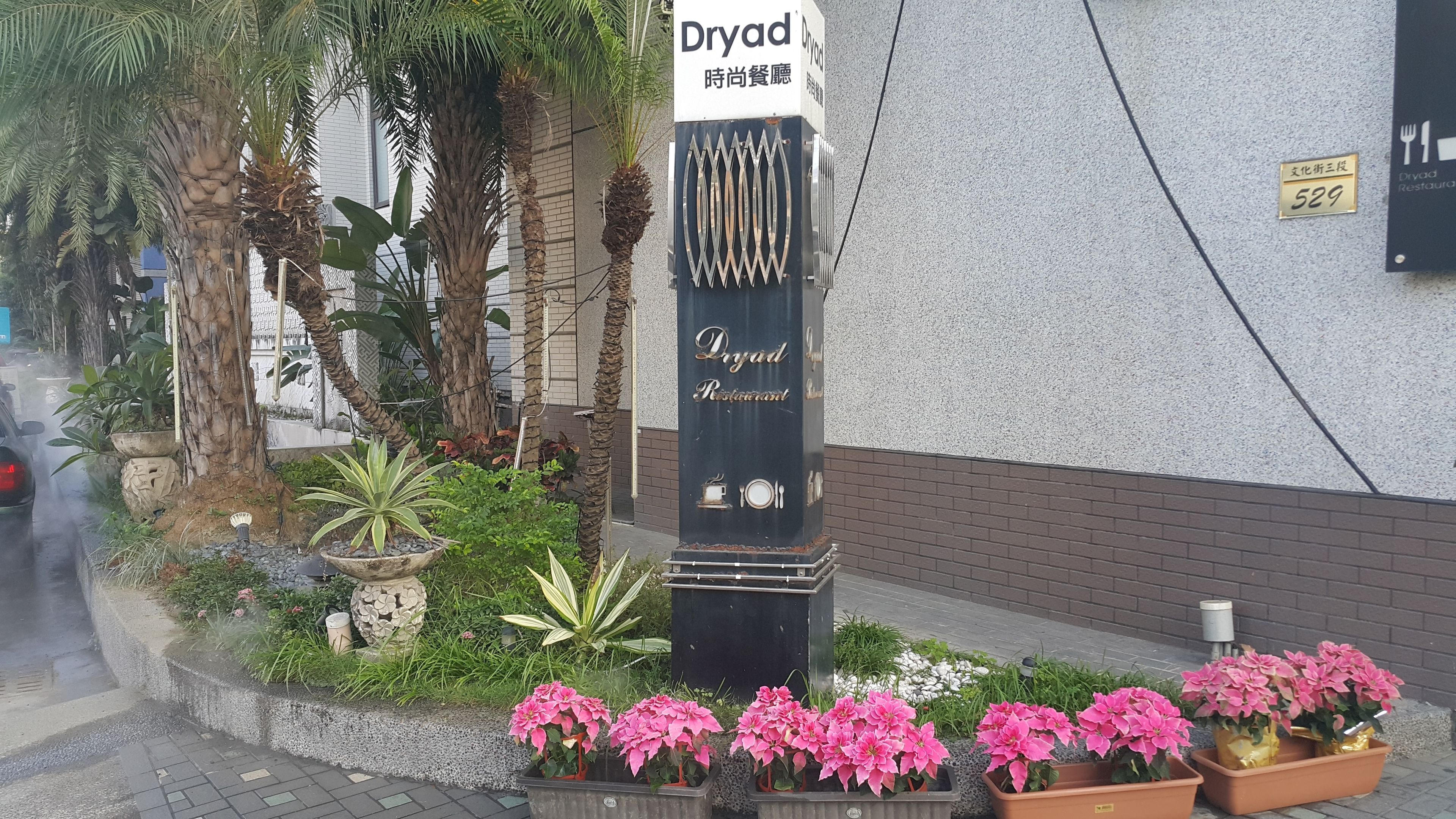 Letrero del Restaurante Dryad con un diseño moderno, rodeado de exuberante vegetación y plantas en macetas.