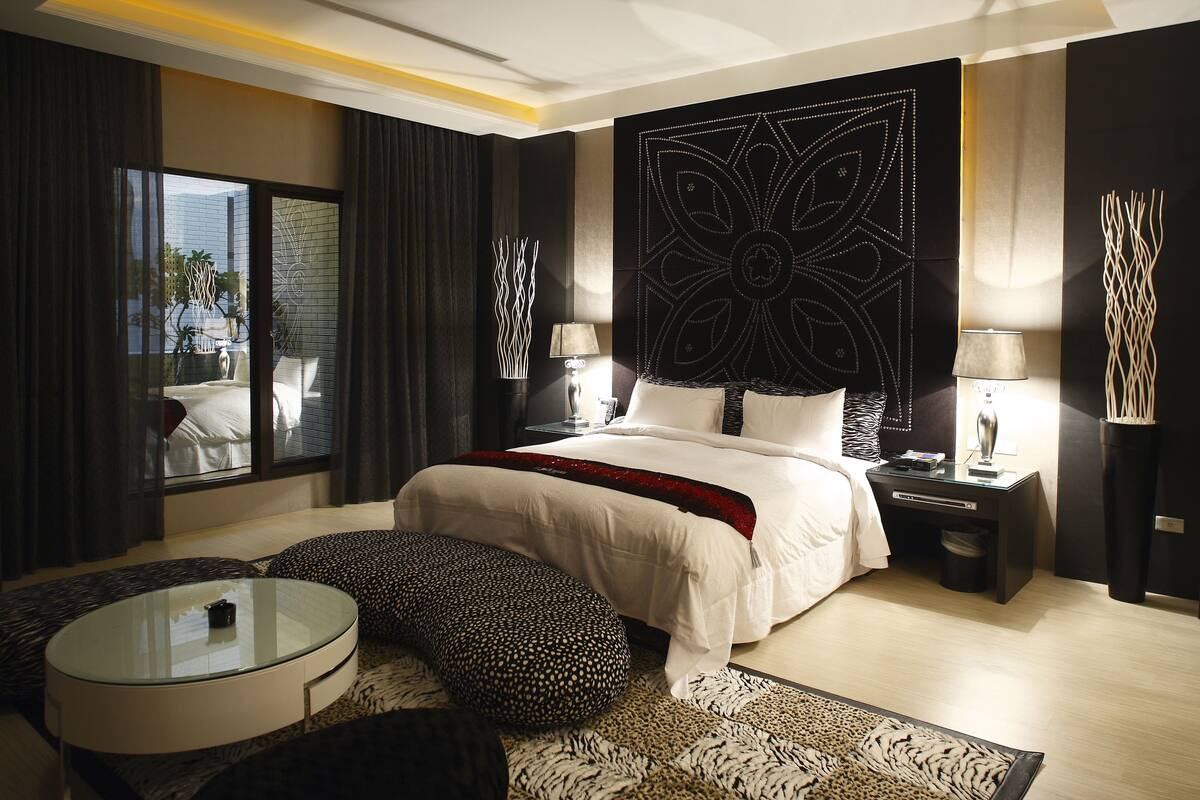 A modern bedroom with a large bed, a glass coffee table, and a view of the outdoors.