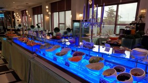 A buffet with various food items displayed in bowls, a candelabra, and a view of the outside through large windows. - Dryad Motel (Tainan)