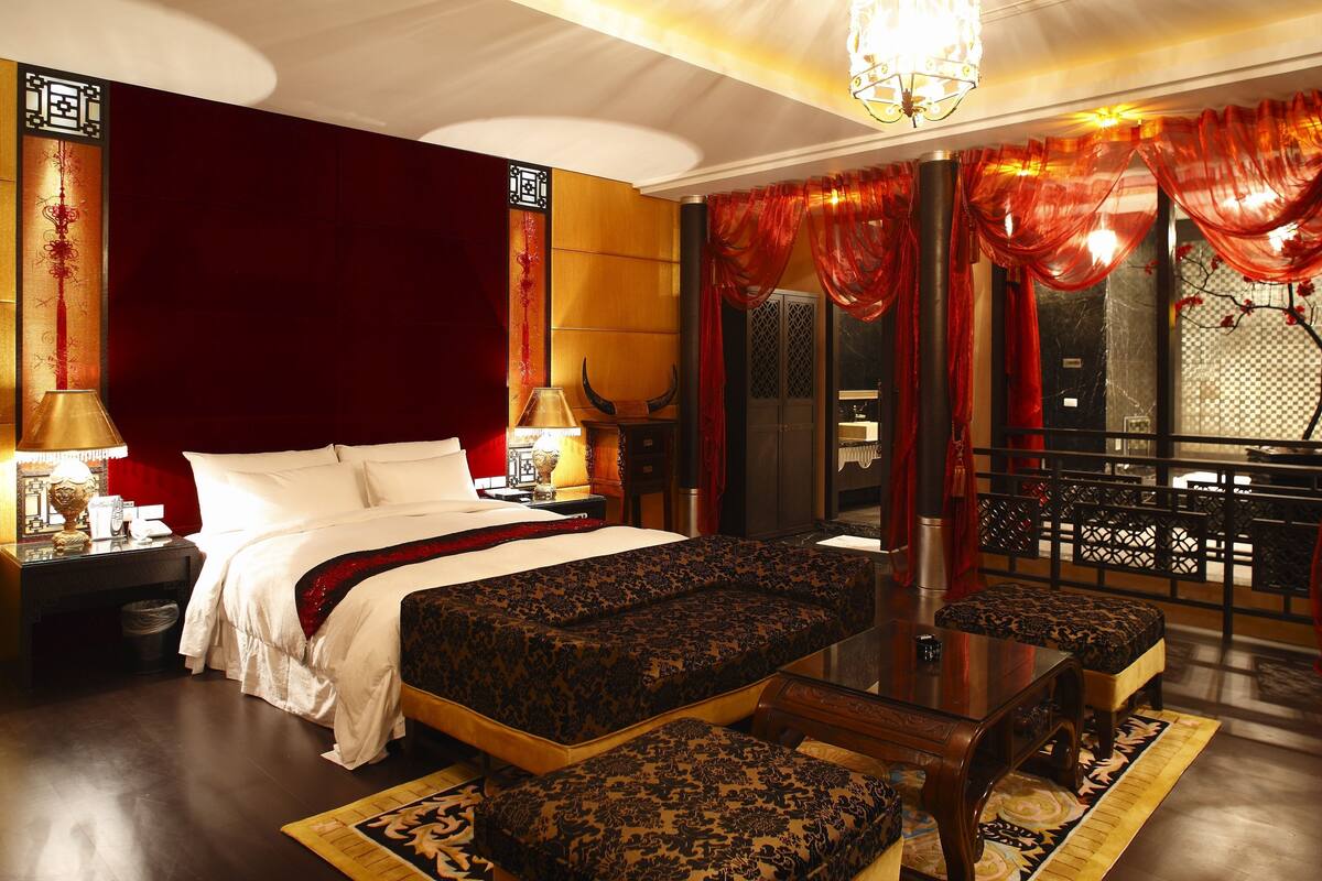A hotel room with a large bed, a small table, and a sofa. There is a window with a view of a balcony.