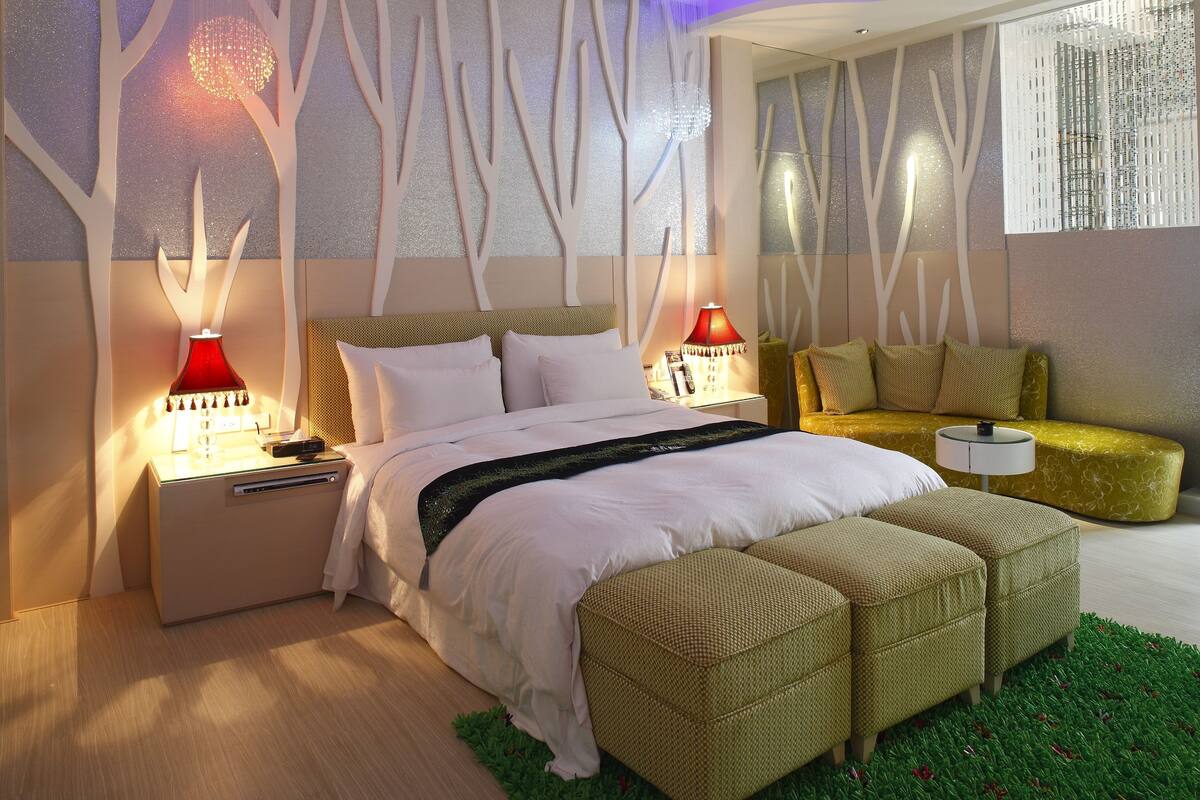 A modern bedroom with a bed, bedside tables, a sofa, and a decorative wall.