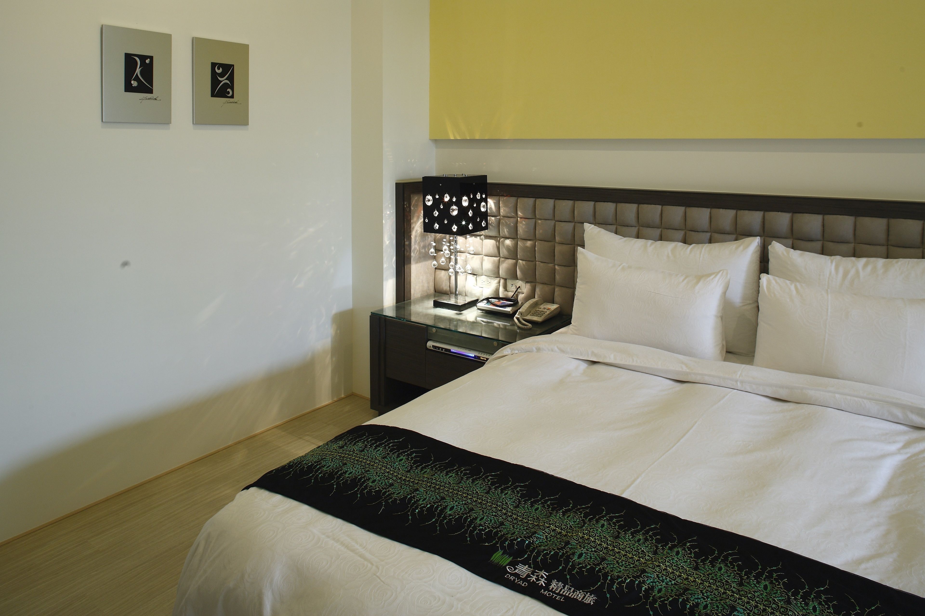 A hotel room with a bed, a nightstand with a lamp, and two framed pictures on the wall.