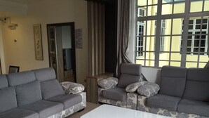 A living room with two grey sofas with floral patterns, a white coffee table, and a large window with curtains. - Cameron Highlands Premier Apartment at Crown Imperial Court (Brinchang)