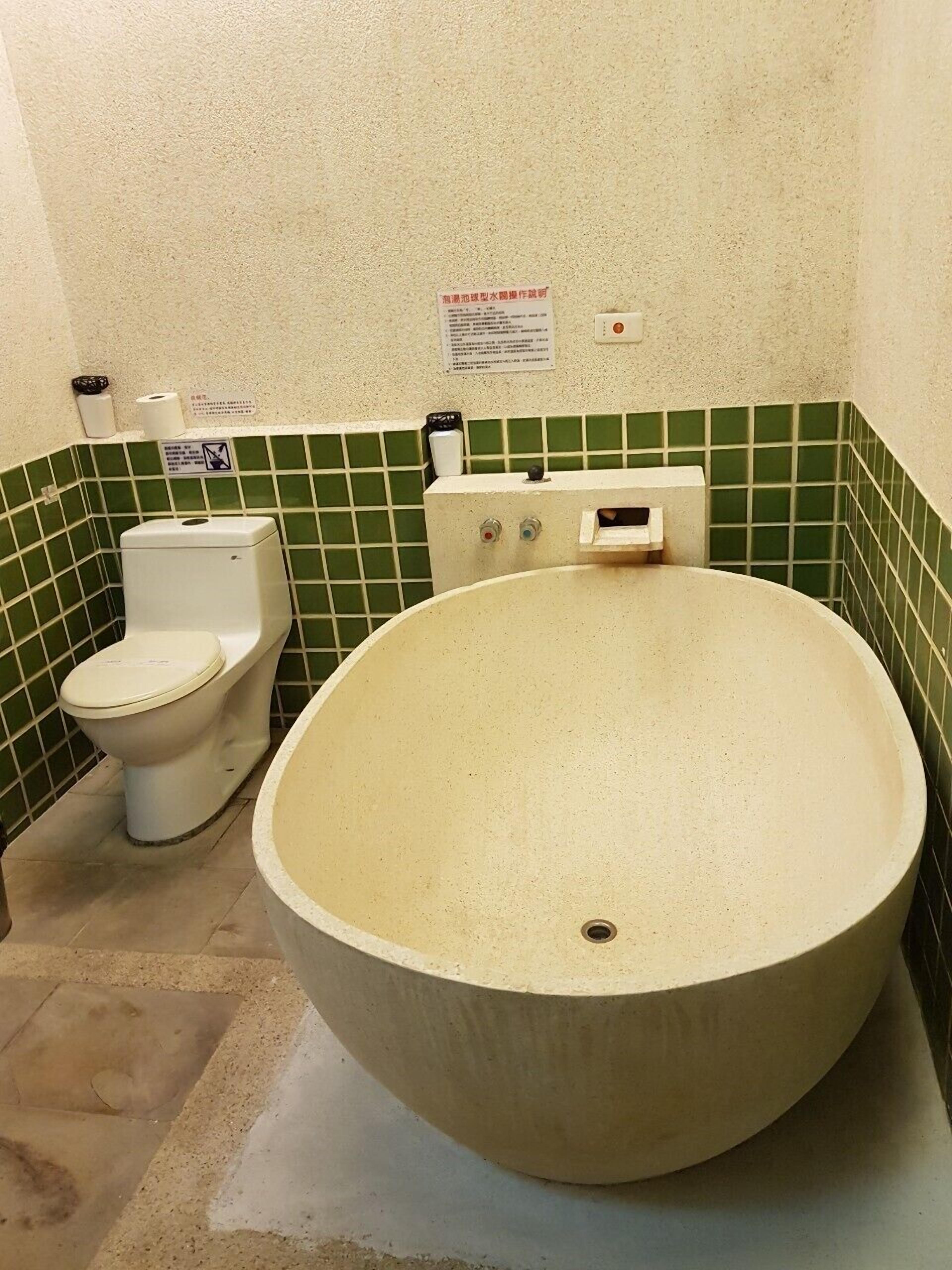 Um banheiro com uma banheira grande, vaso sanitário e parede revestida com azulejos verdes.