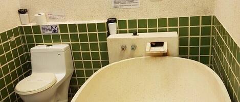 Um banheiro com uma banheira grande, vaso sanitário e parede revestida com azulejos verdes.
