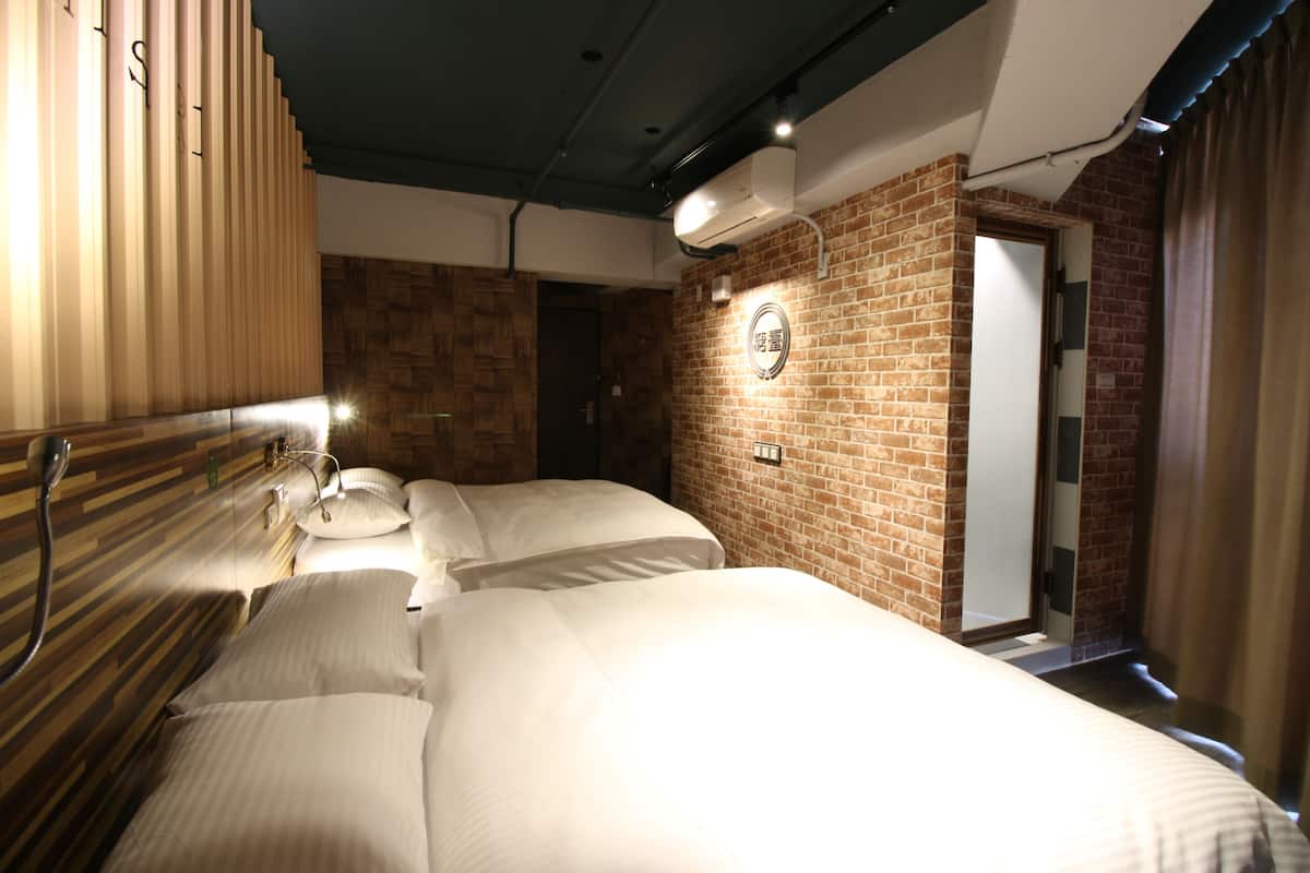 Une chambre d’hôtel avec un mur en briques, une tête de lit en bois et un lit recouvert de draps blancs.