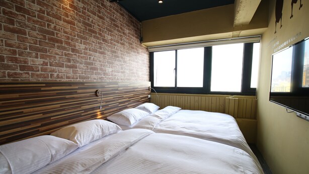 Una habitación de hotel con pared de ladrillo, un ventanal grande y una cama con ropa blanca.