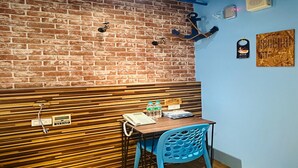 Interior de restaurante con pared de ladrillo, paneles de madera, una silla azul, una mesa con un teléfono y botellas, y un letrero que dice 'Welcome'.