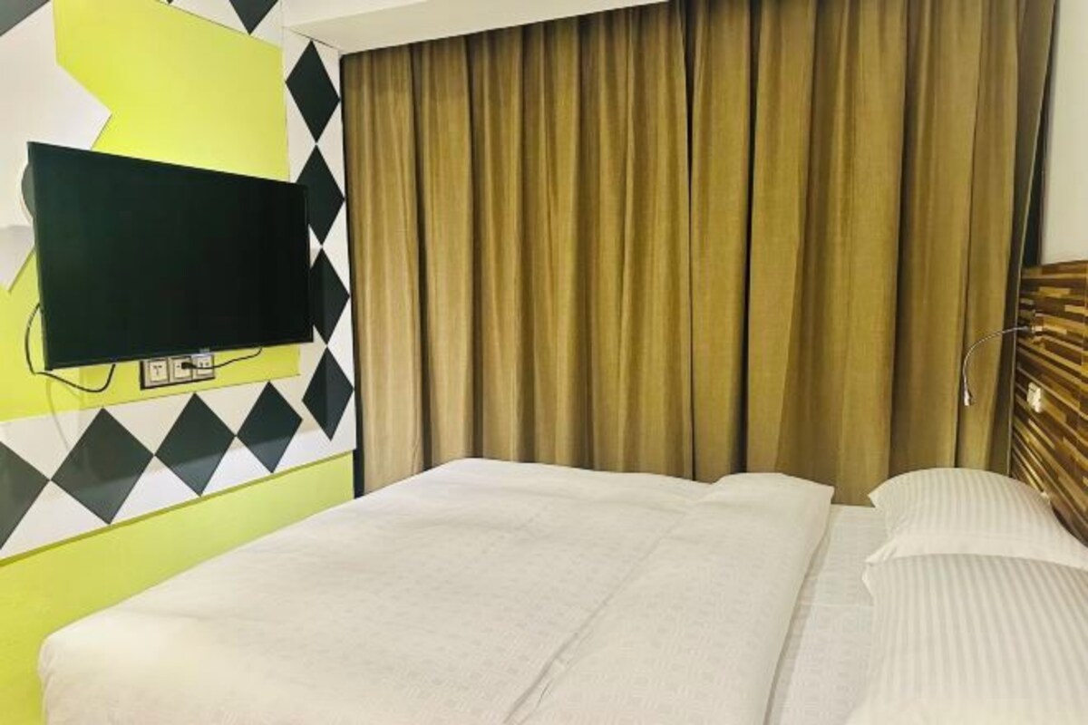 A hotel room with a bed, a television mounted on the wall, and a curtain.