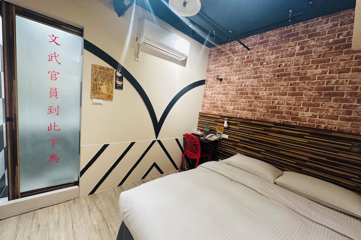 Une chambre d’hôtel avec un lit, un bureau et une chaise, un mur en briques et un ventilateur de plafond.