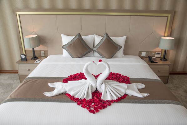 A neatly made bed with a heart-shaped arrangement of towels and rose petals.