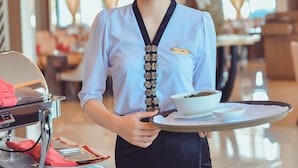 A hotel staff member holding a tray with a bowl and a plate, in a well-lit indoor setting with modern decor. - Muong Thanh Luxury Ca Mau Hotel (Tan Thanh)