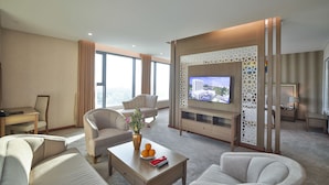 A hotel room with a large TV, comfortable seating, a coffee table with fruit, and a view of the city. - Muong Thanh Luxury Ca Mau Hotel (Tan Thanh)