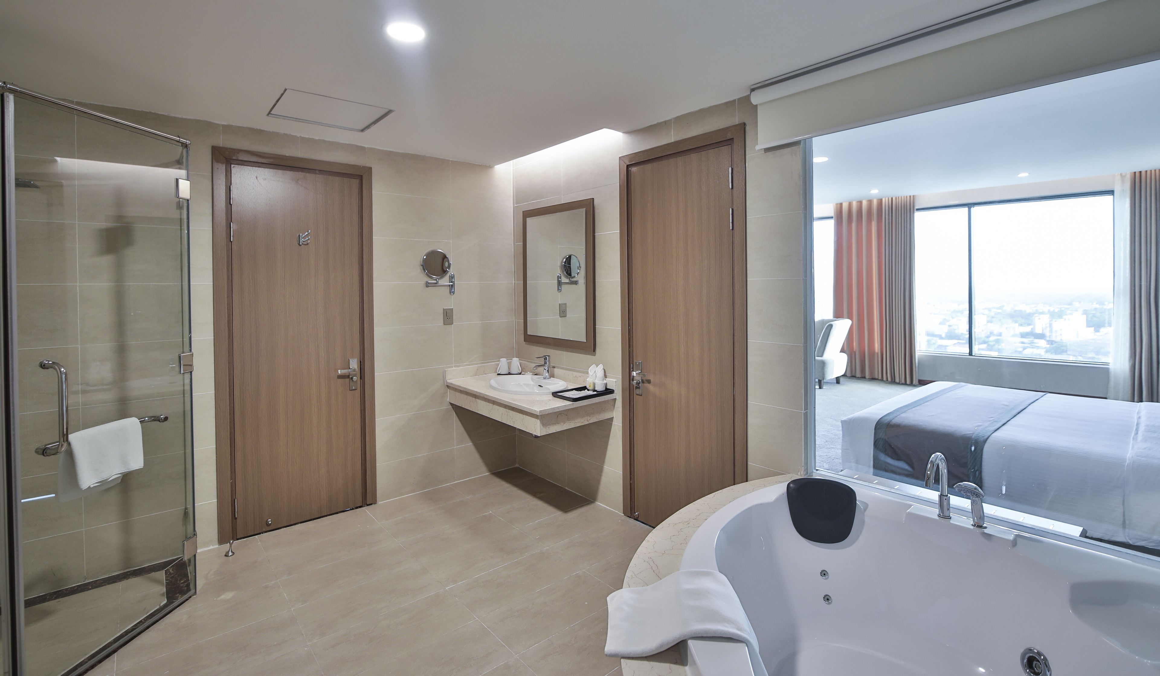A modern hotel bathroom with a glass shower enclosure, a large mirror, a sink with toiletries, and a bathtub.