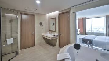 Un baño de hotel moderno con cabina de ducha de vidrio, un espejo grande, un lavabo con artículos de aseo y una bañera.