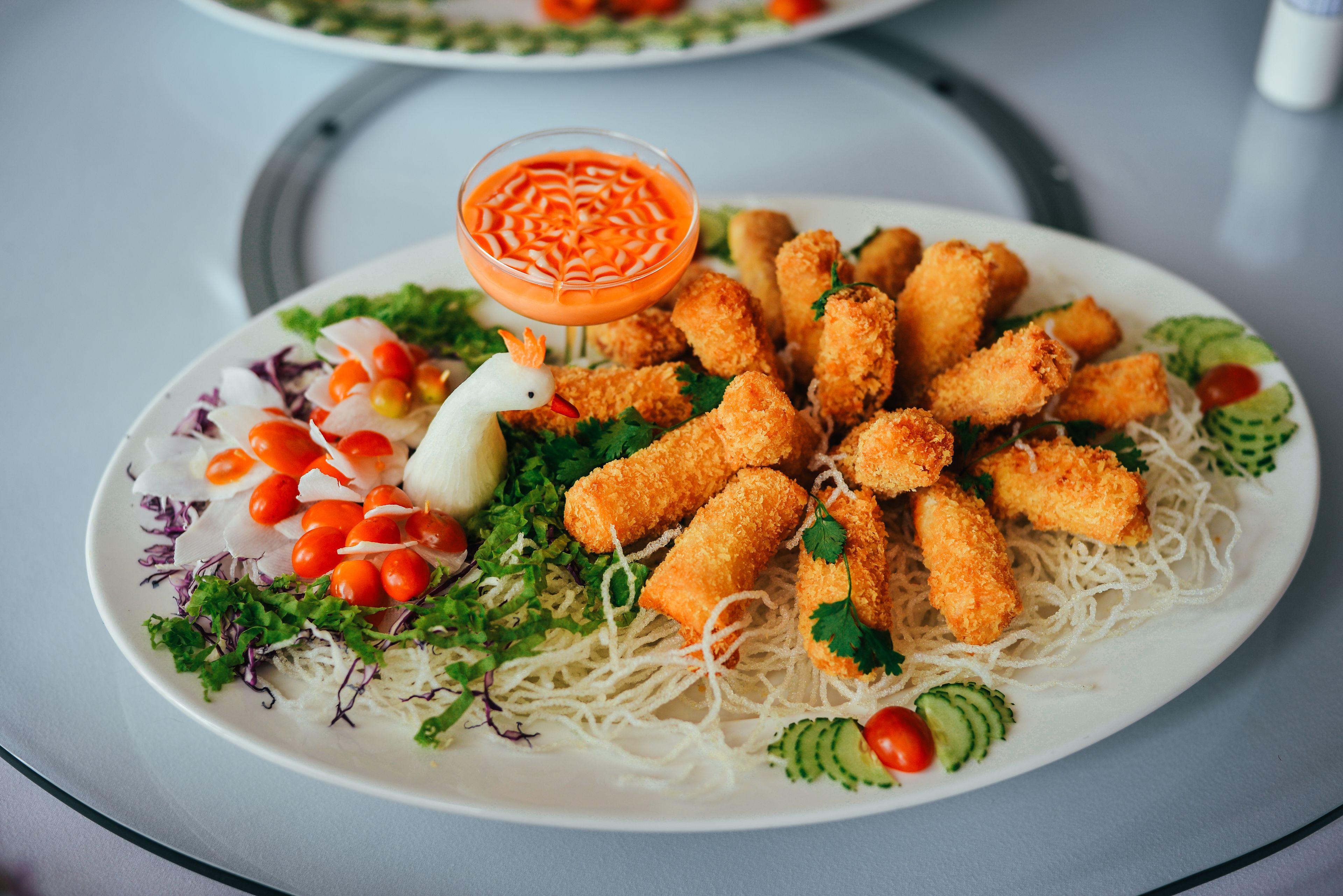 A plate of food with noodles, vegetables, and chicken tenders, accompanied by a dipping sauce.
