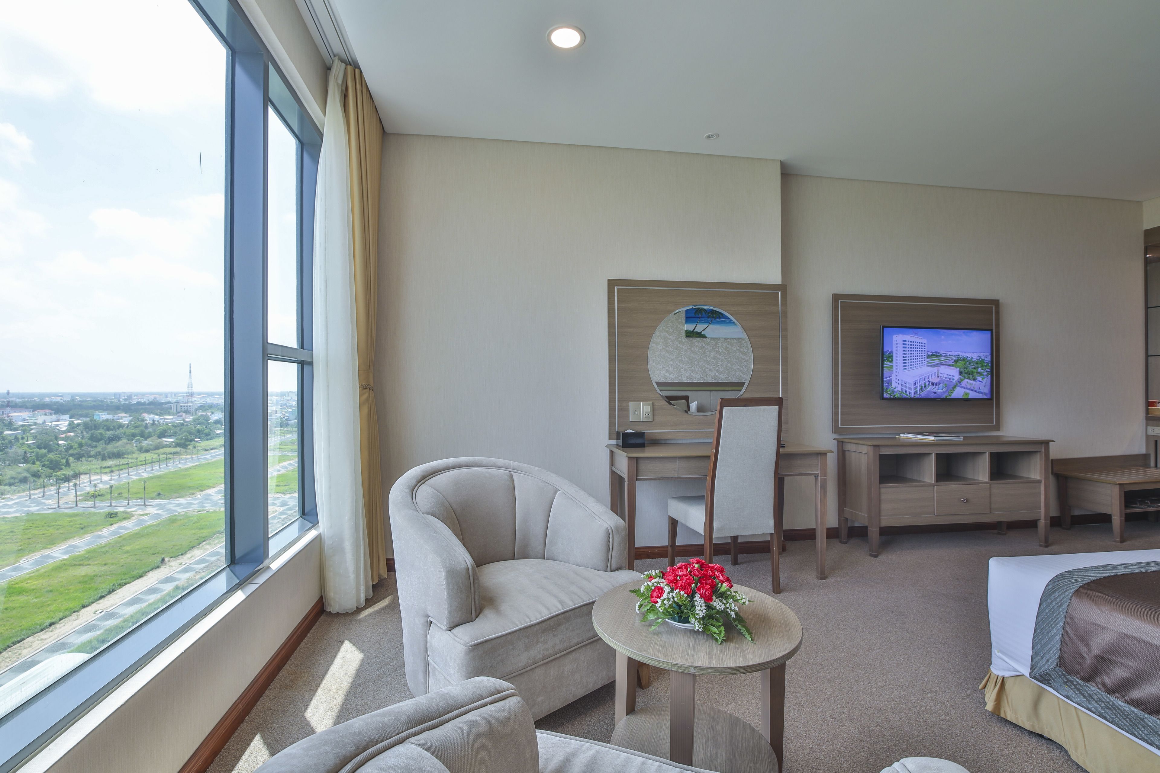 A hotel room with a large window, a bed, a desk, a chair, and a television.