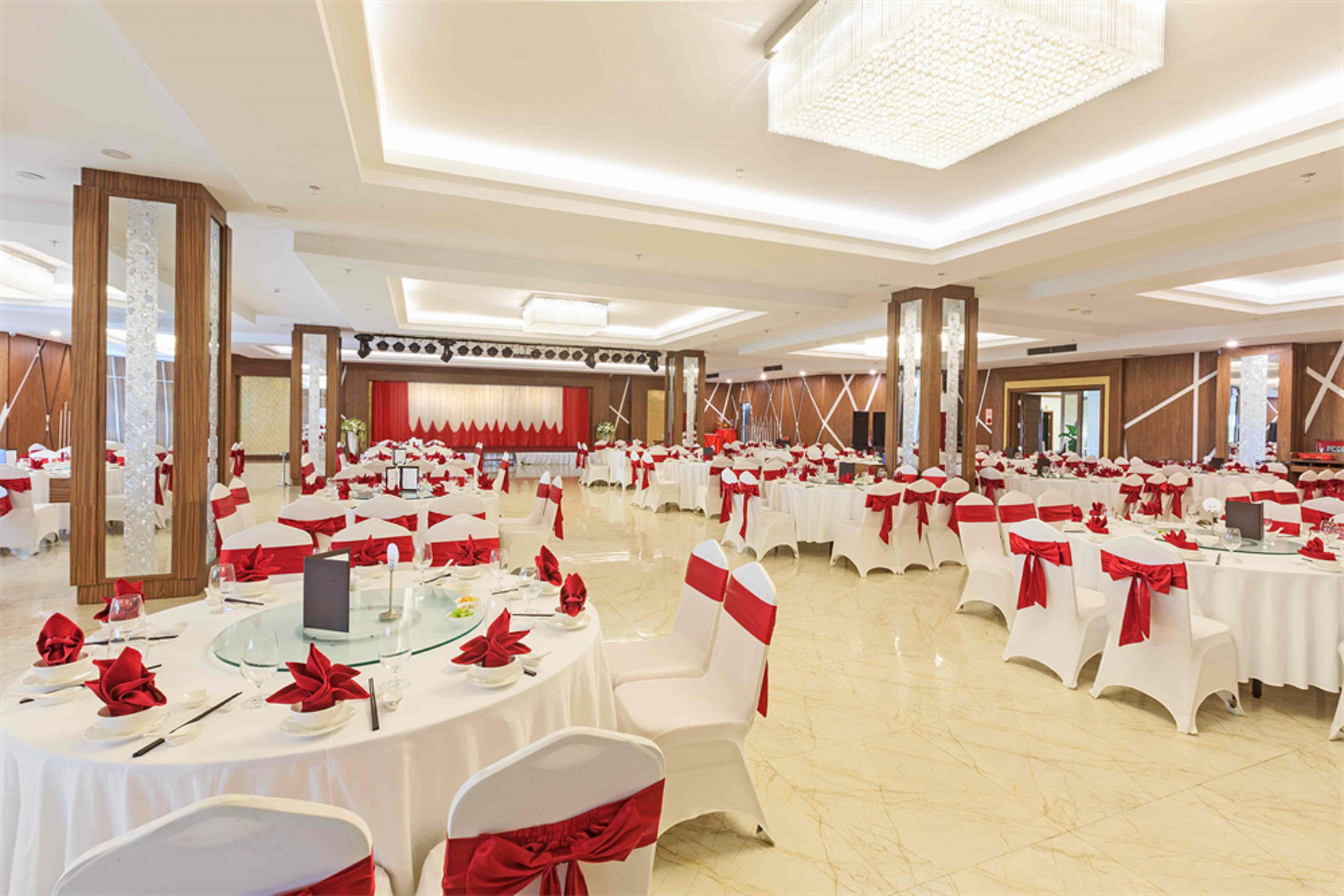 A banquet hall with round tables, white chairs, and red sashes.