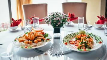 A dining table with two plates of food, a vase of flowers, and red napkins.