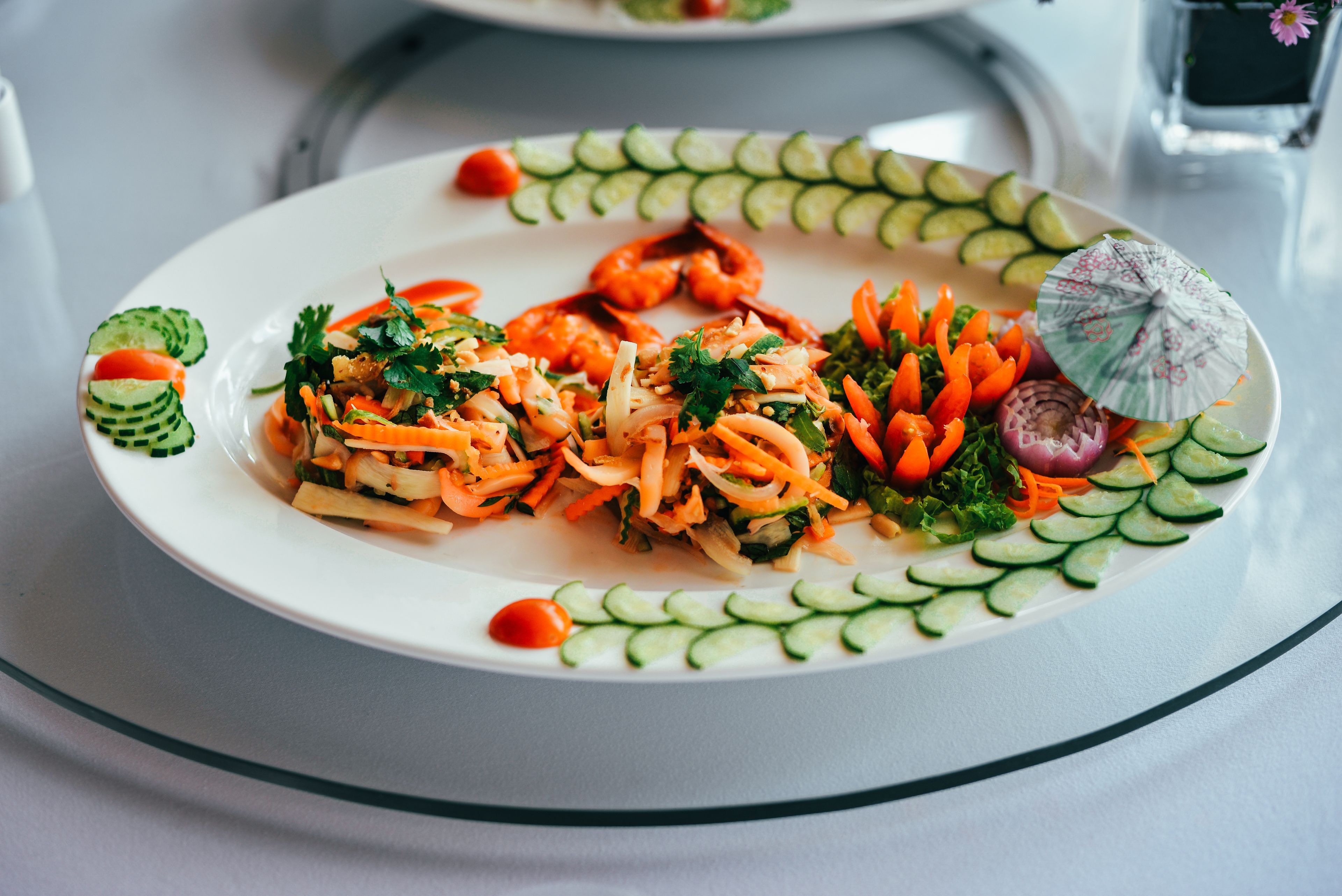 A plate of food with vegetables and shrimp, garnished with herbs and a small umbrella.