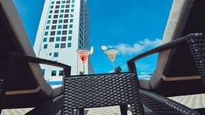 A view from a wicker chair with a high-rise building in the background, a clear blue sky, and two tiki-style lamps. - Muong Thanh Luxury Ca Mau Hotel (Tan Thanh)