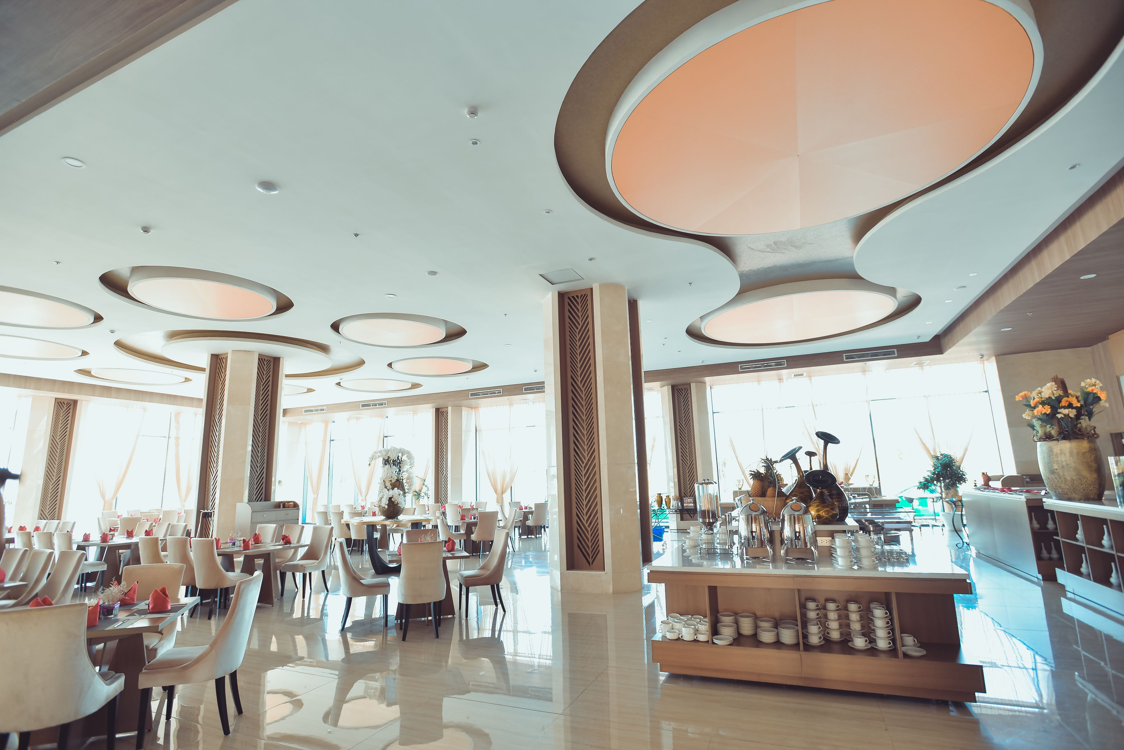 Un hall d’hôtel spacieux au design moderne, doté d’un bar central, de plusieurs espaces aménagés pour s’asseoir et de grandes fenêtres laissant entrer la lumière naturelle.