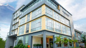 Un hotel moderno con una estructura de varios pisos, amplias ventanas y un área de entrada bien cuidada con plantas.