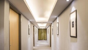 Un pasillo de hotel con cuadros enmarcados en las paredes, una puerta de madera a la izquierda y una cortina verde al final.