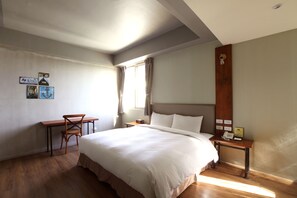 A bedroom with a bed, a desk, and a chair. There is a window with curtains, a nightstand with a phone, and a wall with a wooden panel. - Tourism Inn (Tainan)
