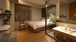 A hotel room with a bed, a chair, a desk with a computer, a mirror, and a bathroom with a sink and toilet. - Tourism Inn (Tainan)