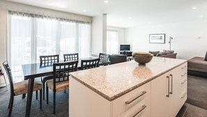 Una cocina moderna con encimera de granito, armarios blancos y una zona de comedor con mesa y sillas.